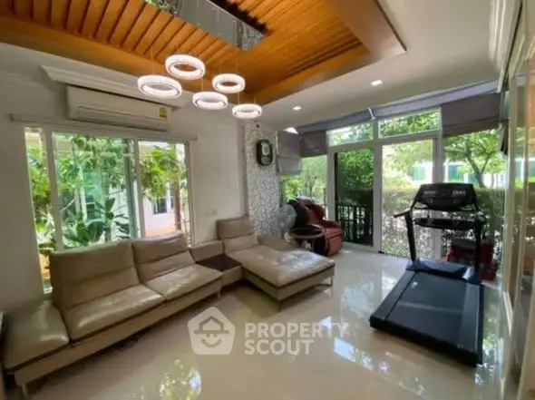 Spacious living room with modern decor and garden view, featuring a treadmill and elegant lighting.