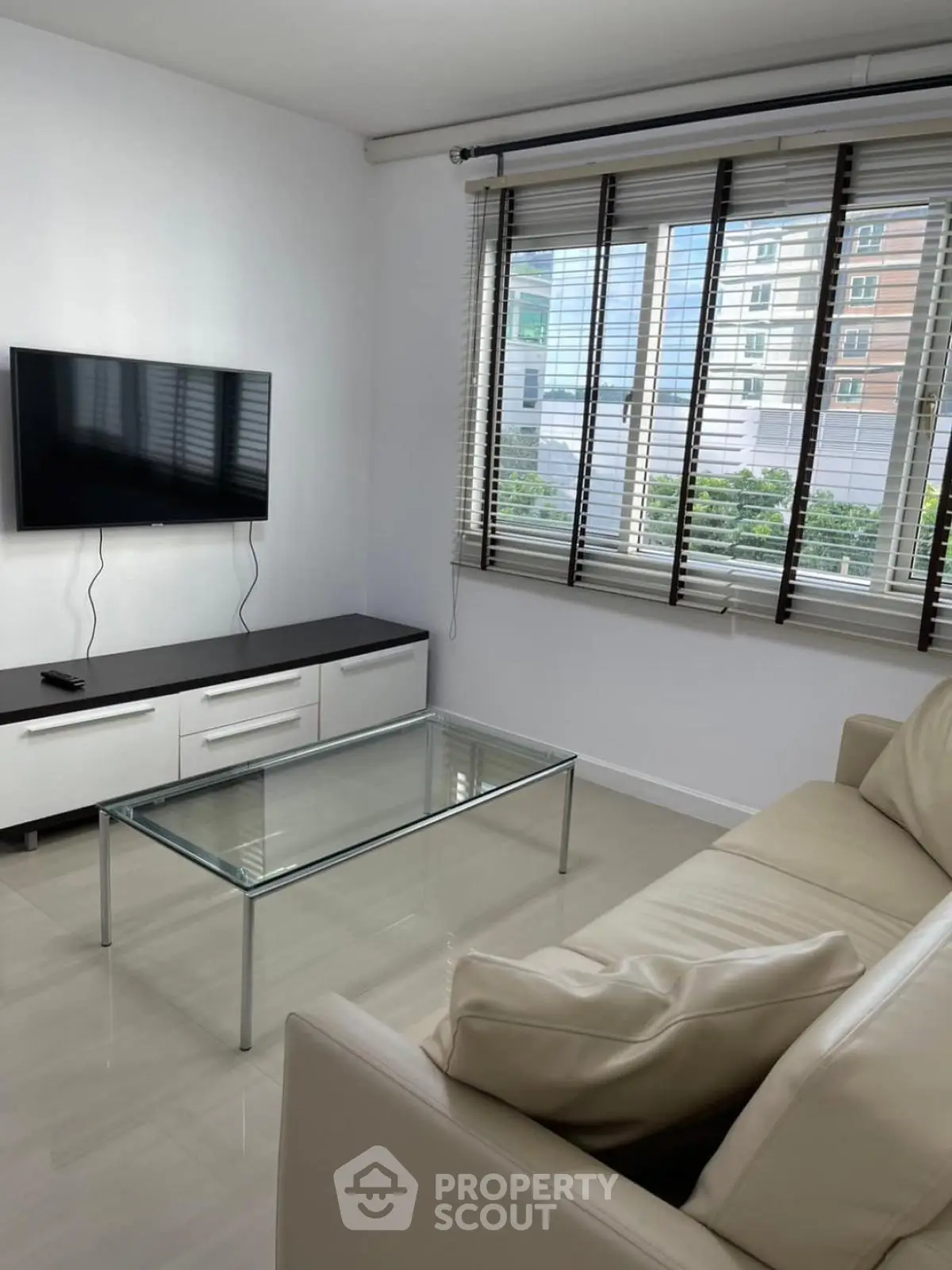 Modern living room with sleek furniture and large window offering city views.