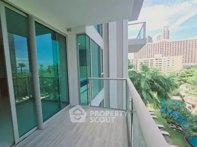 Spacious balcony with glass railing offering stunning city and garden views in a modern high-rise building.