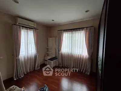 Cozy bedroom with wooden flooring and elegant curtains, featuring air conditioning for comfort.