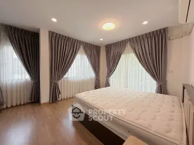 Spacious bedroom with elegant curtains and natural light, featuring a comfortable bed and wooden flooring.