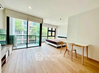 Spacious modern studio with large windows and balcony in urban setting.