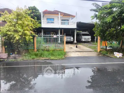 Charming two-story house with balcony and driveway in a lush suburban setting.
