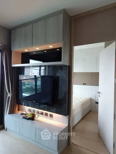 Modern living room with sleek TV unit and view into stylish bedroom.
