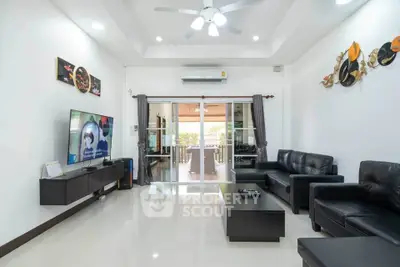 Spacious modern living room with sleek black furniture and large TV, leading to a bright balcony view.