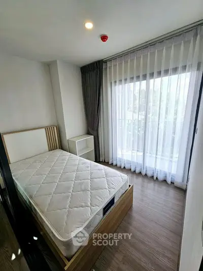 Bright bedroom with large window and modern decor, featuring a comfortable bed and elegant curtains.
