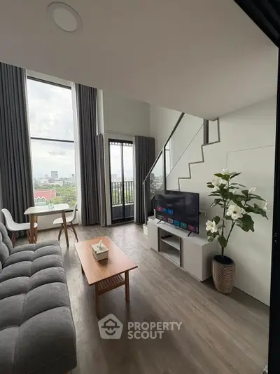 Modern living room with high ceilings, large windows, and stylish decor in a city apartment.
