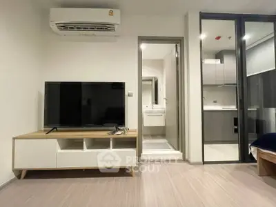 Modern living room with sleek TV stand and air conditioning, adjacent to a compact kitchen and bathroom.