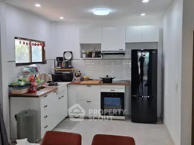 Modern kitchen with sleek black fridge and white cabinetry, featuring a cozy and functional layout.