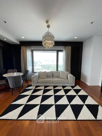 Elegant living room with modern chandelier and geometric rug, featuring a cozy sofa and dining area.