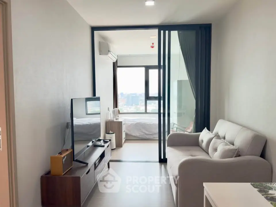 Modern living room with sliding glass doors and city view, featuring cozy sofa and sleek TV stand.
