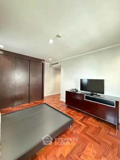 Spacious bedroom with wooden flooring and modern furniture, featuring a sleek TV setup.