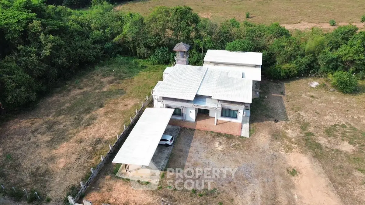 Aerial view of a modern house with spacious yard and carport in a serene rural setting.