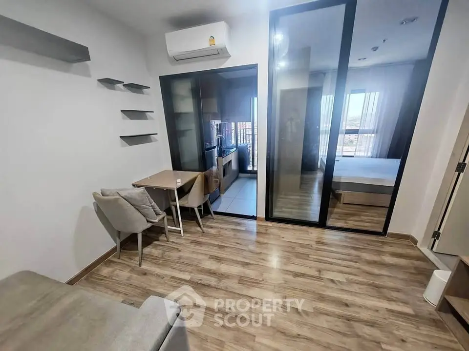Modern studio apartment with glass partition, wooden flooring, and compact kitchen area.