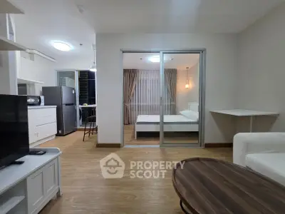 Modern open-plan living room with adjacent bedroom, featuring sleek furniture and wooden flooring.