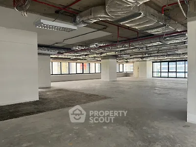 Spacious open-plan commercial space with large windows and exposed ceiling pipes.