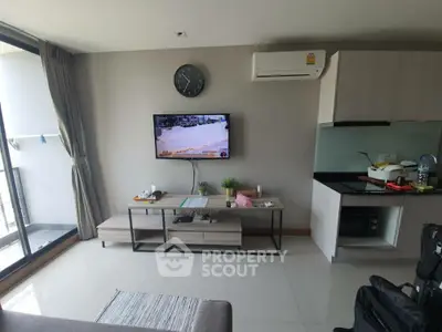 Modern living room with TV and kitchen area, featuring sleek design and natural light.