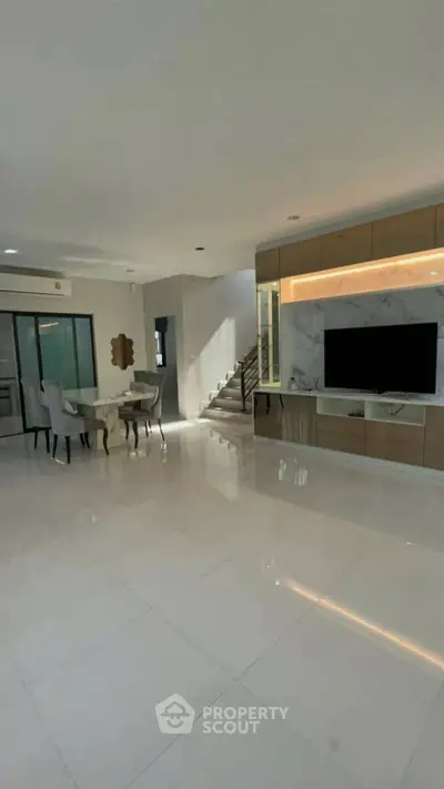 Spacious modern living room with sleek design and elegant dining area, featuring a large TV and stylish staircase.