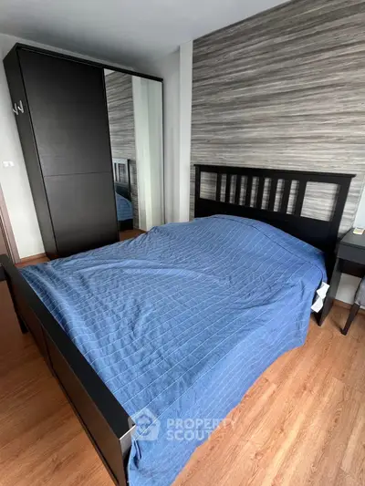 Modern bedroom with stylish wooden flooring and sleek black furniture, featuring a cozy bed and mirrored wardrobe.
