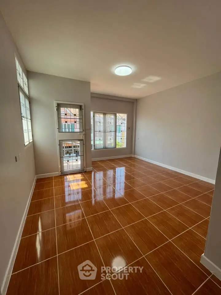 Spacious sunlit room with glossy tiled flooring and large windows in modern apartment.