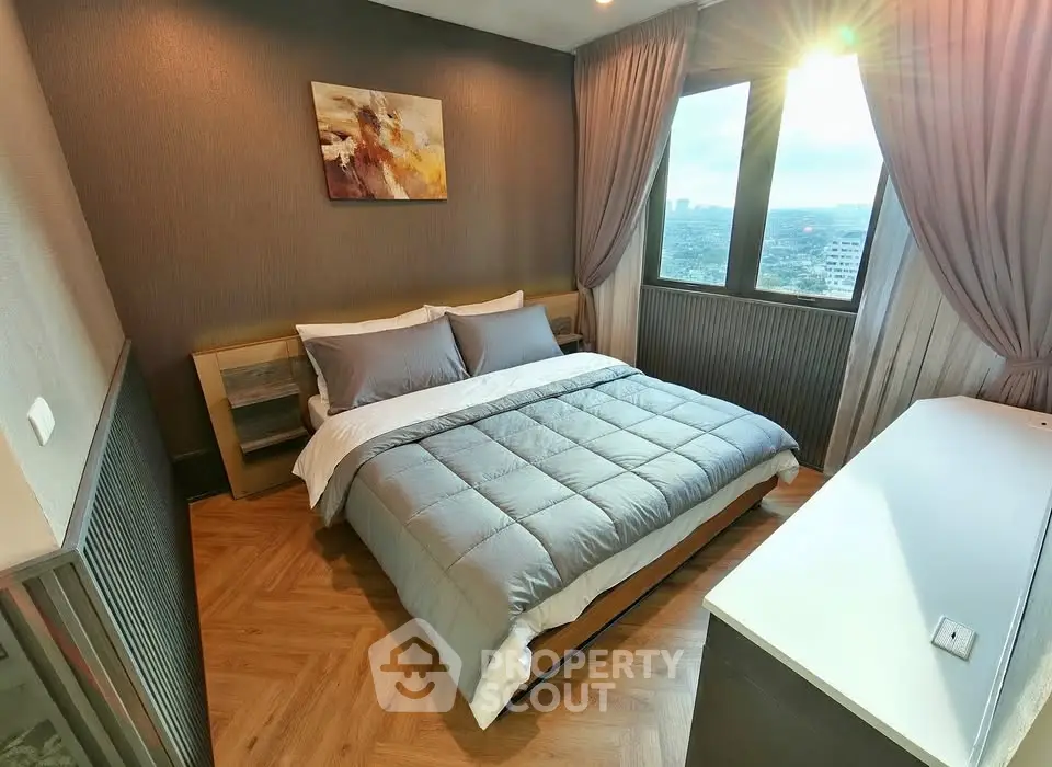 Modern bedroom with cozy bedding and city view from large windows.