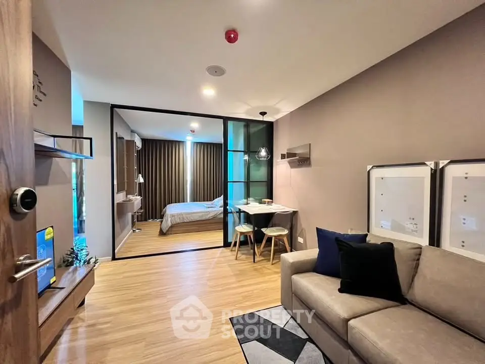 Modern apartment interior with open living room and bedroom, featuring stylish decor and wooden flooring.