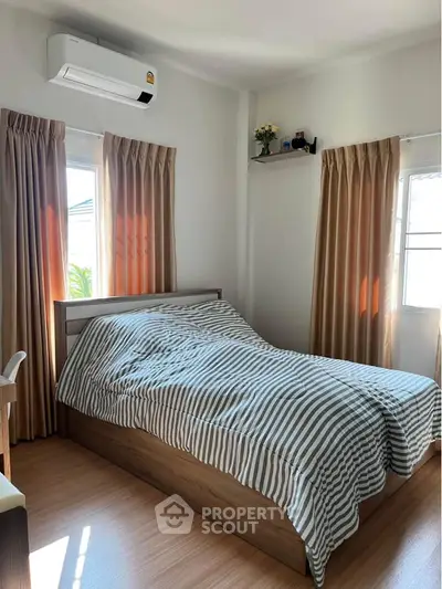 Cozy bedroom with striped bedding and natural light, featuring air conditioning and wooden flooring.