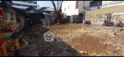 Vacant urban lot with potential for development, surrounded by buildings and featuring a tree and motorbikes.
