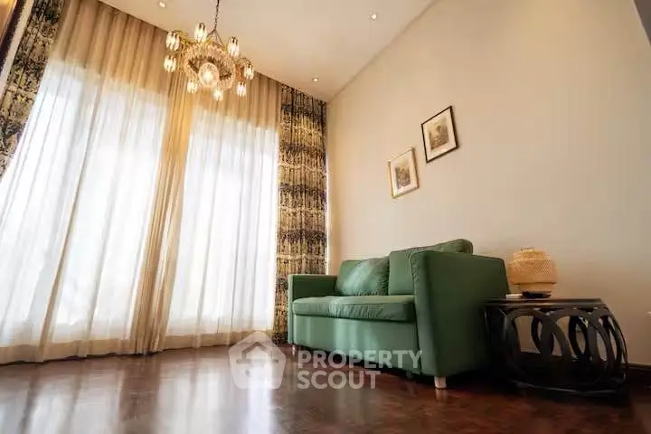 Elegant living room with green sofa, stylish chandelier, and floor-to-ceiling curtains.