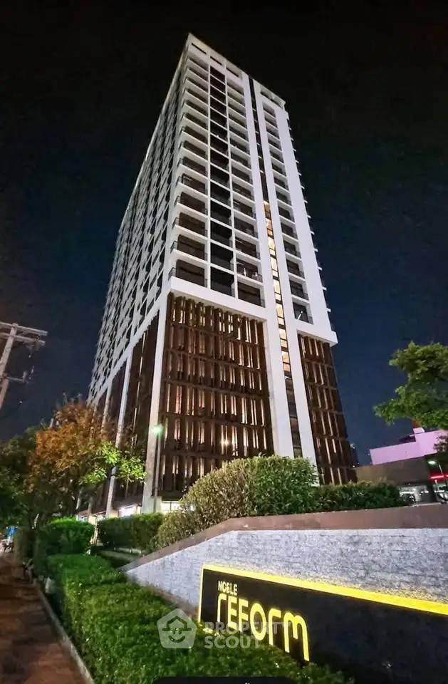 Stunning night view of a modern high-rise building with lush landscaping, perfect for urban living.