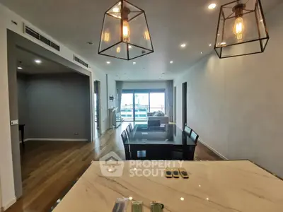 Spacious modern dining area with elegant lighting and open layout, featuring a view of the balcony.