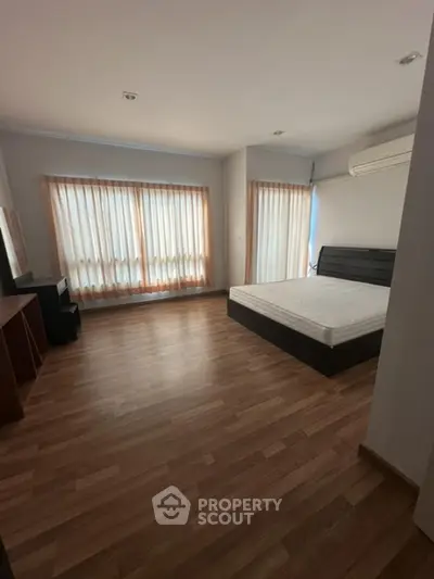 Spacious bedroom with wooden flooring and large windows for natural light
