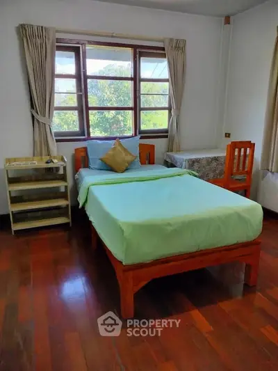Cozy bedroom with wooden flooring and large window offering a scenic view, perfect for relaxation.