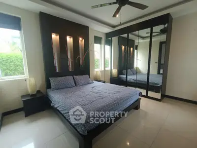 Spacious bedroom with modern decor and mirrored wardrobe, featuring large windows and ceiling fan.