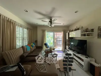 Cozy living room with large sofa, ceiling fan, and entertainment center overlooking garden view.