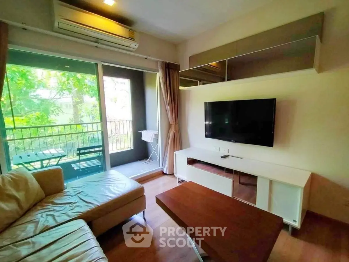 Modern living room with large window and balcony view, featuring sleek furniture and air conditioning.