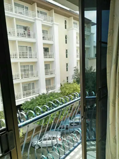Charming balcony view of modern apartment building with lush greenery and parked cars.
