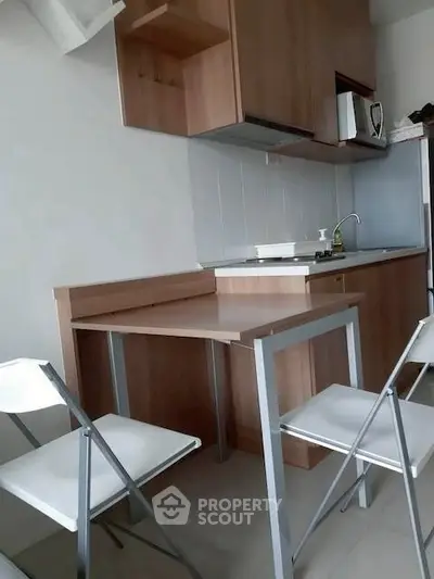 Modern compact kitchen with wooden cabinets and foldable chairs, ideal for small apartments.