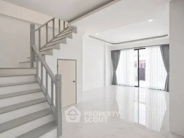 Spacious modern living room with elegant staircase and large windows for natural light.