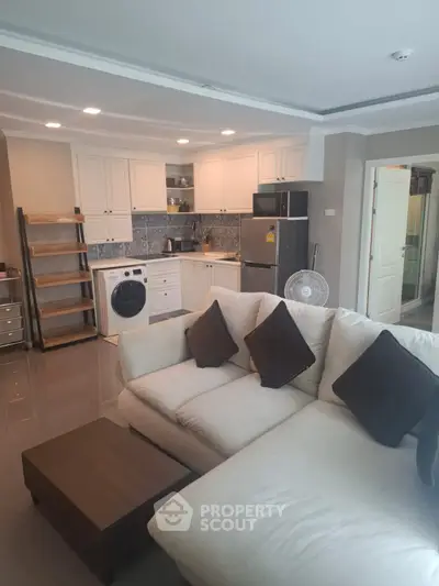 Modern open-layout living room with kitchen, featuring sleek appliances and cozy seating area.