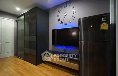 Modern living room with sleek design, featuring a wall clock, TV, and stainless steel fridge.