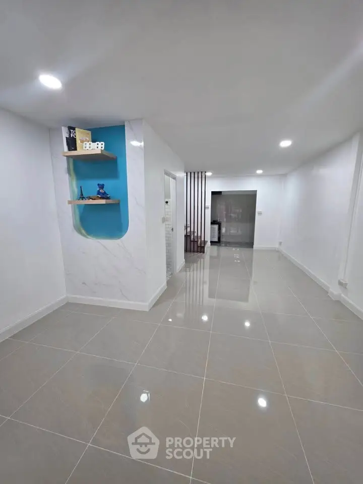 Spacious modern living room with glossy tiled floors and stylish wall shelves, perfect for contemporary living.