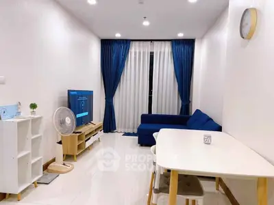 Modern living room with blue sofa, TV, and dining table in a bright apartment.