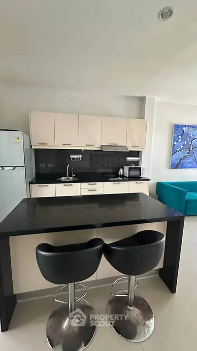 Modern kitchen with sleek black countertop and stylish bar stools in a contemporary apartment.