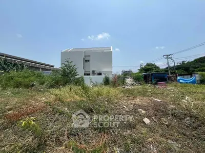 Spacious land plot with modern white building and lush greenery, ideal for development opportunities.