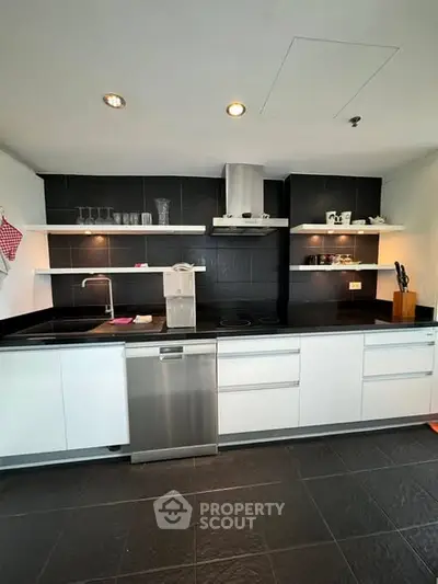Modern kitchen with sleek white cabinetry and black countertops, featuring built-in appliances and open shelving.
