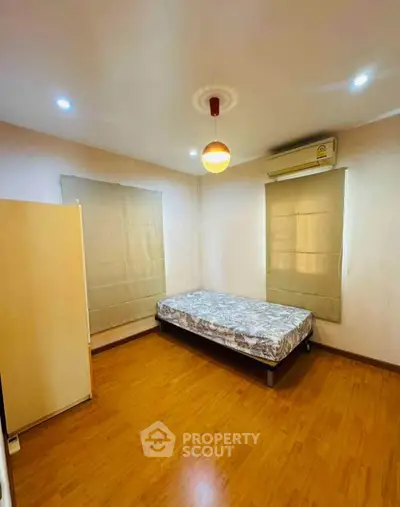 Cozy bedroom with wooden flooring and minimalist decor, featuring a single bed and air conditioning.