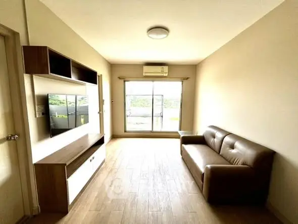 Bright living room with modern sofa and wall-mounted TV unit, featuring large window for natural light.