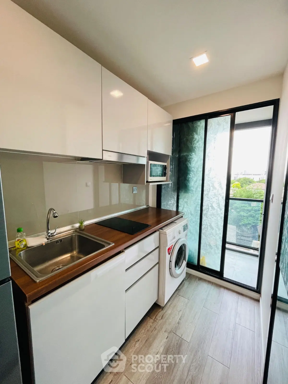 Modern kitchen with sleek design, featuring washing machine and balcony view.