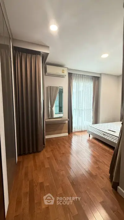 Spacious bedroom with wooden flooring and large windows in modern apartment